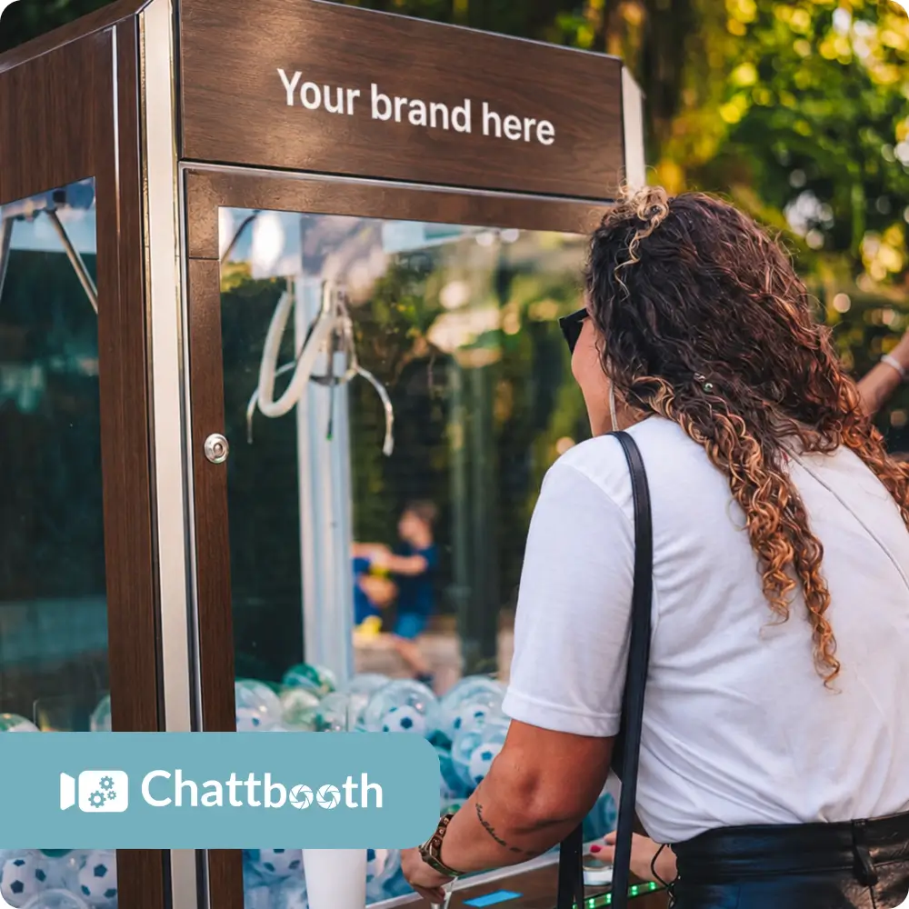 Guest playing a custom branded claw machine with the Chattbooth logo at an outdoor event